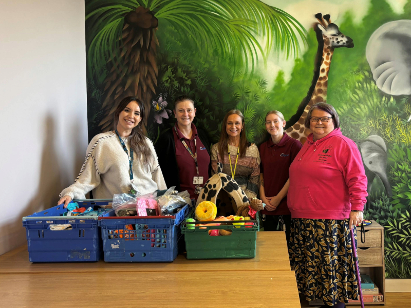 A group of staff standing behind tables displaying crates of donated pet supplies, including toys, blankets and food, in front of a colourful wildlife mural.
