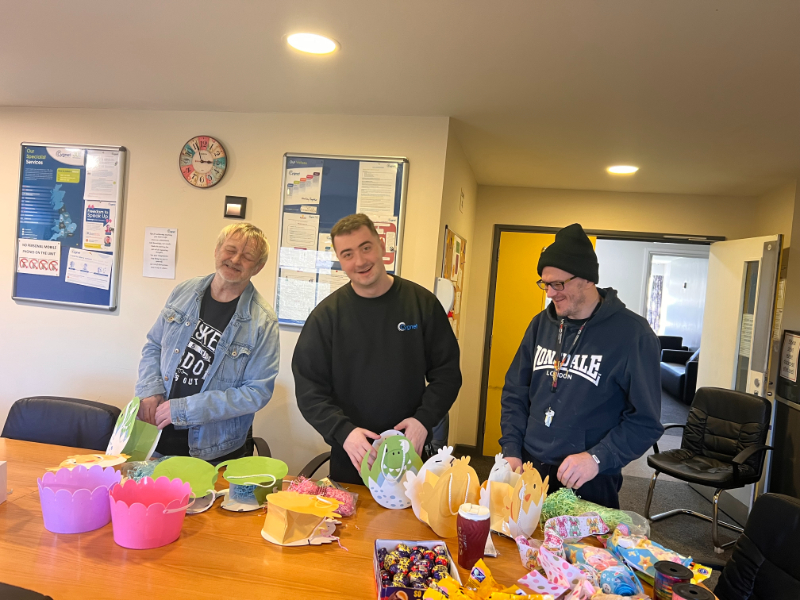 Three people standing around a table at Cygnet Sherwood House, smiling while taking part in Easter arts and crafts.