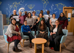 The Cygnet Hospital Sheffield team smiling to celebrate the retention of the Triangle of Care in the reception holding stars and the accreditation logo